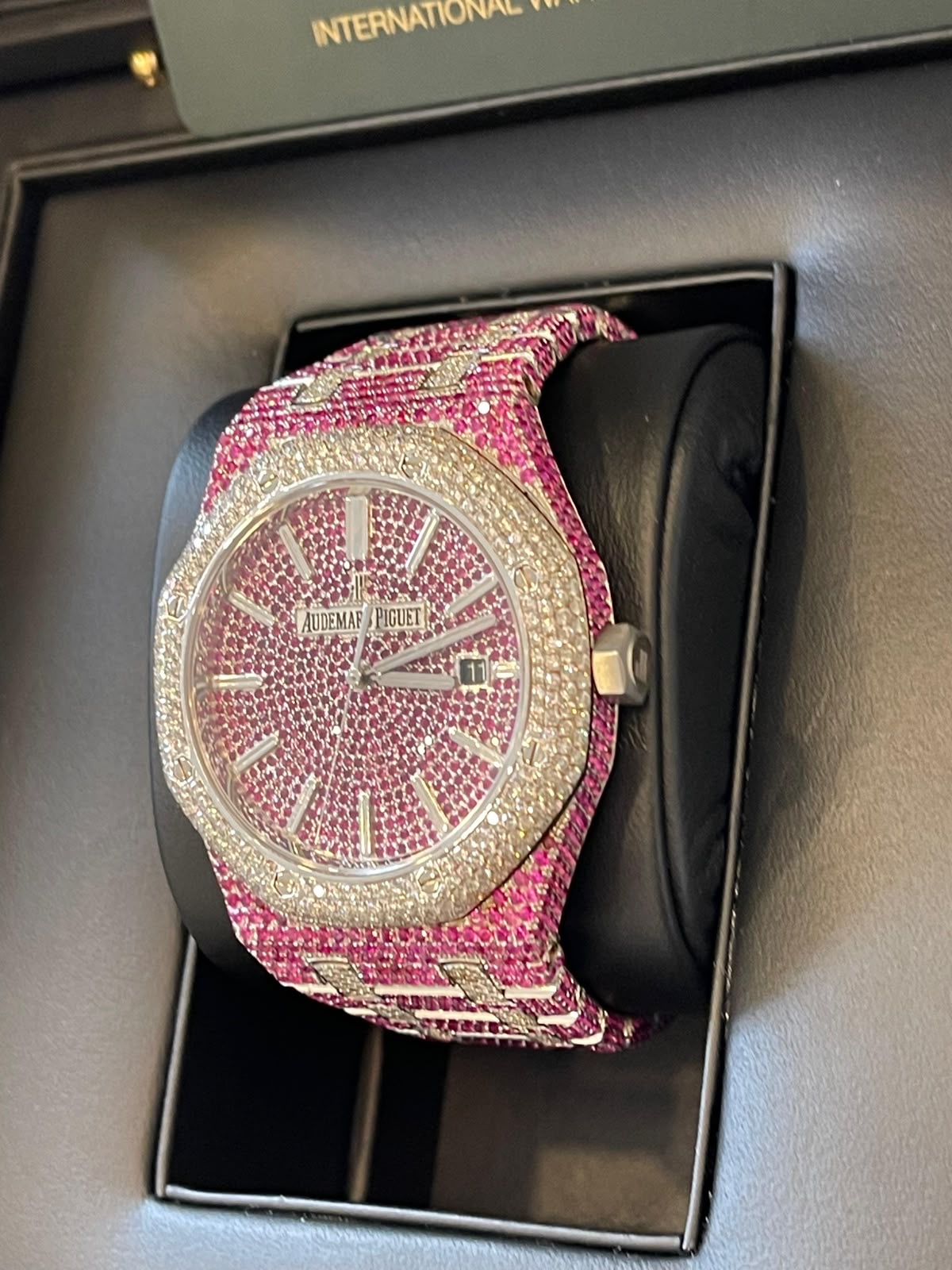 Rosa diamantbesetzte Uhr auf dunklem Uhrenkissen